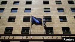 A European Union flag (L) flutters next to a Greek flag on the facade of the Bank of Greece headquarters in Athens, April 14, 2015.