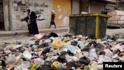 বিদ্রোহীরা উত্তরাঞ্চলীয় প্রধান শহর আলেপ্পো দখল করার পর আবর্জনার স্তূপের পাশ দিয়ে নারীরা হেঁটে যাচ্ছেন। ৪ ডিসেম্বর, ২০২৪।