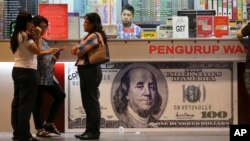 Customers check exchange rates on Malaysian ringgit at a foreign currency money-changer in Kuala Lumpur, Malaysia on Monday, Aug. 24, 2015. (AP Photo/Vincent Thian)
