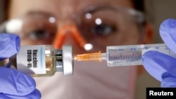 FILE - A woman holds a small bottle labeled with a "Vaccine COVID-19" sticker and a medical syringe in this illustration taken April 10, 2020.