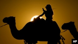 A woman looks at her photo while riding a camel in Mesaieed, Qatar, Nov. 26, 2022. (AP Photo/Ashley Landis)