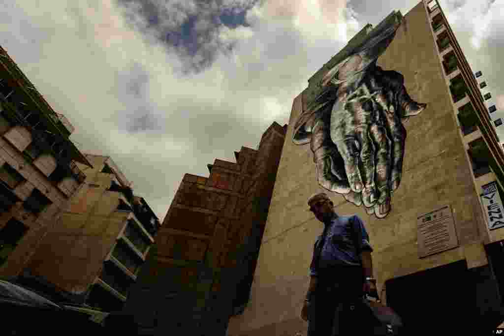 A man walks down a street with a turned upside-down mural inspired by &quot;The Praying Hands&quot; by Renaissance artist Albrecht Durer, in Athens. The bitter standoff between Greece and its international creditors was extended into the weekend, just days before Athens has to meet a crucial debt deadline.