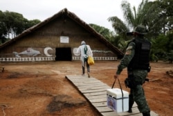 FILE - A municipal health worker and an environmental military police officer carry the AstraZeneca/Oxford vaccine as they enter an Indigenous hut at the Tupe Sustainable Development Reserve in Manaus, Brazil, Feb. 9, 2021.