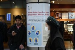 FILE - A woman wearing a face mask passes a Public Health England sign, warning arriving passengers that the coronavirus has been detected in Wuhan in China, at Terminal 4 of London Heathrow Airport in west London on Jan. 28, 2020.