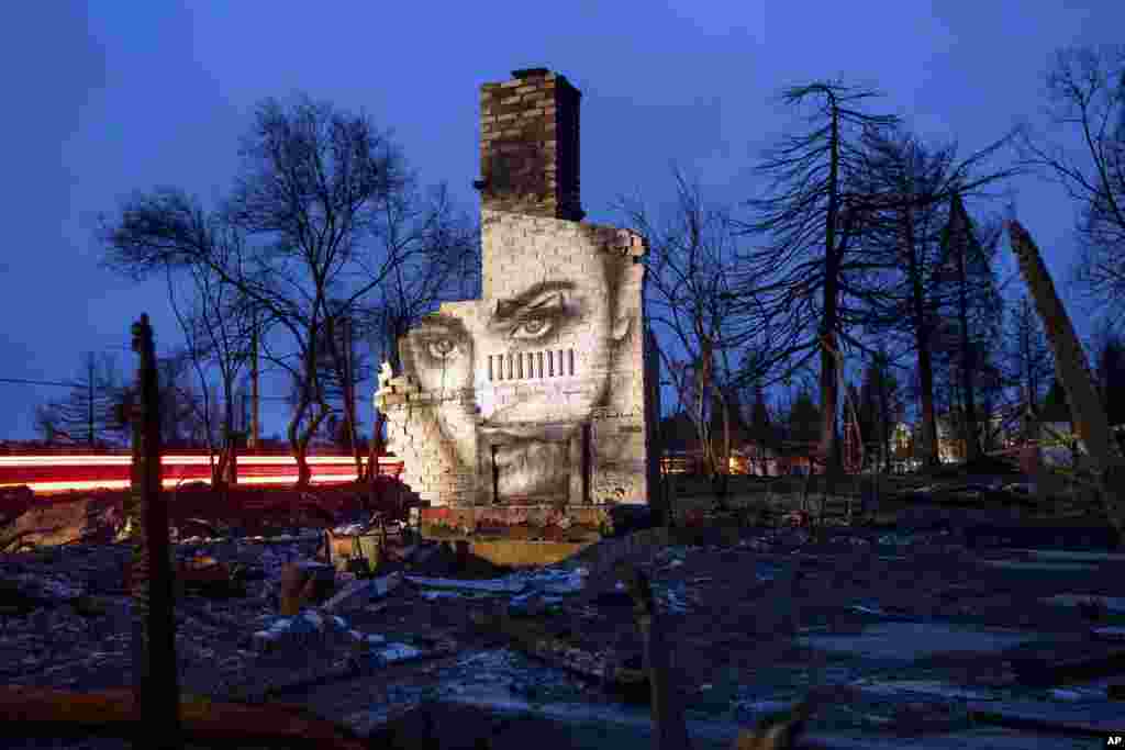 A picture glows as the sun sets on February 8, 2019, in Paradise, a town in the American state of California. An artist painted the image on this and other burned homes in the area after a fire destroyed most of the town. (AP Photo/Noah Berger)