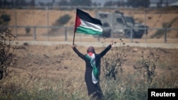 A woman holding a Palestinian flag gestures in front of Israeli forces during a protest marking the 71st anniversary of the 'Nakba', or catastrophe, at the Israel-Gaza border fence, in the southern Gaza Strip, May 15, 2019.