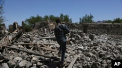 Seorang polisi keamanan Afghanistan berjalan di atas reruntuhan rumah yang hancur setelah operasi di Asad Khil, dekat lokasi pengeboman AS di distrik Achin Jalalabad, timur Kabul, Afghanistan, Sabtu, April 17, 2017.(AP Photo/Rahmat Gul)