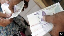 A man working at a money exchange passes 100 Cambodian riel notes to a client in central Phnom Penh, file photo.