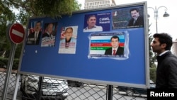 A man passes an election poster with portraits of presidential candidates in central Baku, October 4, 2013.