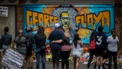 FILE - People are seen gathered at a memorial featuring a mural of George Floyd, near the spot where he died while in police custody, in Minneapolis, Minnesota, May 31, 2020.