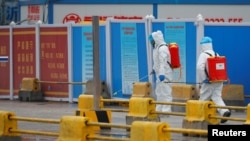 Pekerja dengan menggunakan APD menyemprot tanah dengan diinfektan di pasar Baishazhou selama kunjungan tim Organisasi Kesehatan Dunia (WHO) yang bertugas menyelidiki asal usul pandemi COVID-19, di Wuhan, Provinsi Hubei. (Foto: Reuters)