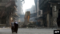 Syrians walk past anti-sniper curtains remaining in a street on May 12, 2014 in a destroyed neighbourhood of the Old City of Homs.