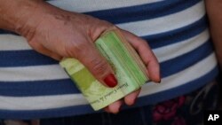 FILE - A woman holds a wad of bills to pay her bus fare in Caracas, Venezuela, Feb. 7, 2018. 