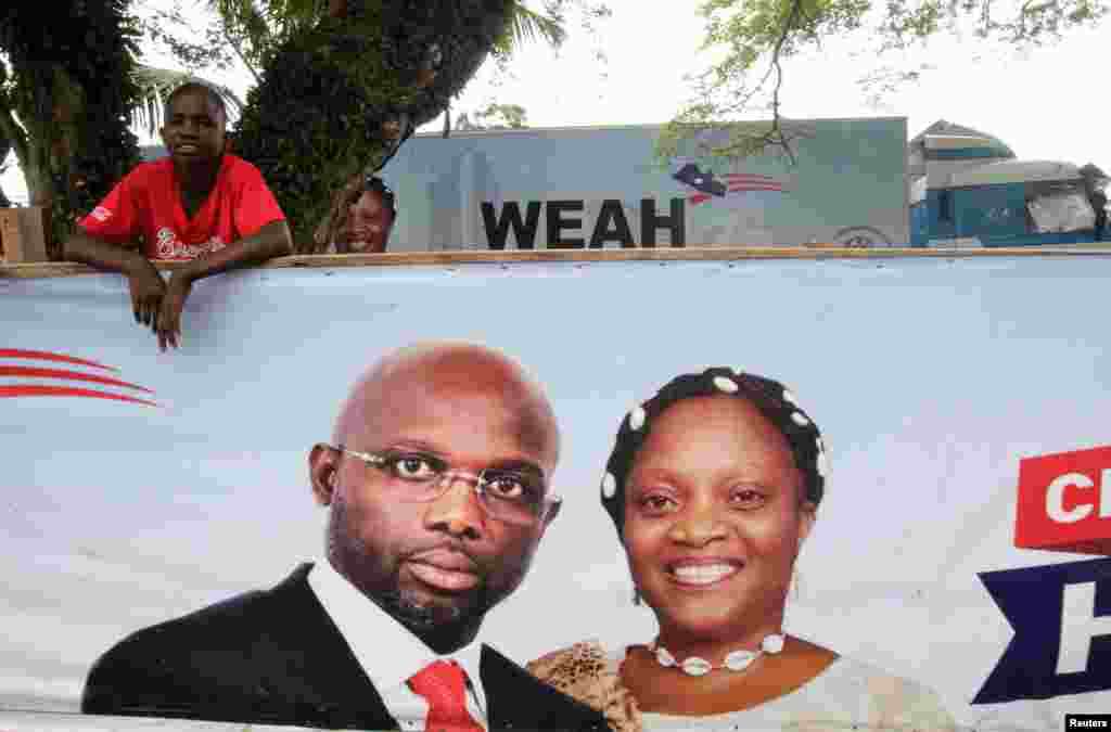 A supporter of former soccer player and presidential candidate of Congress for Democratic Change (CDC) George Weah stands behind a presidential campaign banner in Monrovia, Oct. 6, 2017.