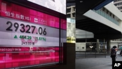 A woman walks past a bank's electronic board showing the Hong Kong share index at Hong Kong Stock Exchange in Hong Kong, Jan. 19, 2021.