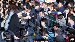 Jaksa dan media mengelilingi Choi Soon-sil (tengah, menunduk, menggunakan topi hitam), orang dekat Presiden Korea Selatan Park Geun-hye yang ada di pusat skandal korupsi, di kantor Kejaksaan Distrik Seoul (31/10). (AP/Lee Jin-man)