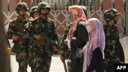 Perempuan etnis Muslim Uighur melewati polisi paramiliter China yang sedang berpatroli di sebuah jalan di Urumqi, ibu kota wilayah Xinjiang China pada 3 Juli 2010. (Foto: AFP)