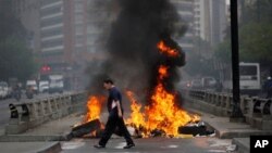 Seorang pejalan kaki berjalan melewati barikade yang sengaja dibakar demonstran anti-pemerintah untuk memblokir jalan besar di Chacao, Caracas, Venezuela, (24/2). 