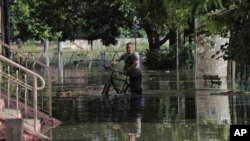 Seorang warga tampak mendorong sepedanya di jalan yang banjir di wilayah Kherson, Ukraina, pada 6 Juni 2023. Banjir hinggap di sejumlah wilayah di Ukraina akibat bendungan Kakhovka yang hancur. (Foto: AP/Nina Lyashonok)