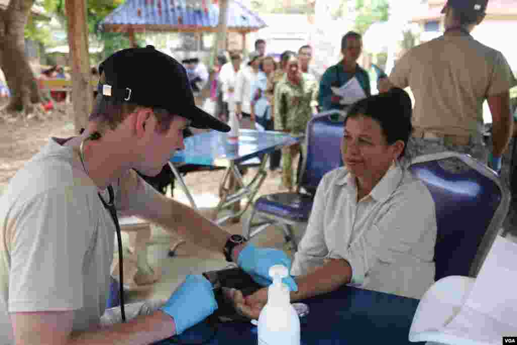 មន្ត្រី​កងទ័ពអាកាសសហរដ្ឋអាមេរិកម្នាក់ពិនិត្យសម្ពាធឈាមស្រ្តីមួយរូប នៅស្រុកកំពង់ត្រាច ខេត្តកំពត កាលពីថ្ងៃពុធ ទី១៥ ខែមិថុនា ឆ្នាំ២០១៦។&nbsp;