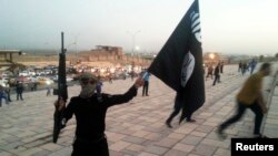 Seorang pejuang Negara Islam (ISIS) memegang bendera ISIS dan senjata di Mosul, Irak.