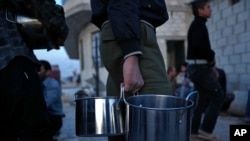 FILE - Syrians who were displaced with their families from eastern Ghouta hold their pots as they wait to receive food from the main kitchen at a shelter in the village of Horjelli, in the Damascus countryside, April 13, 2018.