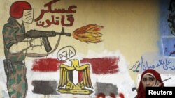 A woman sits in front of a wall filled with graffiti against the Supreme Council of the Armed Forces near Tahrir Square in Cairo, June 5, 2012.