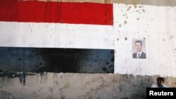 A man sits near a poster of Syrian President Bashar al Assad during the re-opening of the road between Homs and Hama in Talbisi, Syria June 6, 2018. 