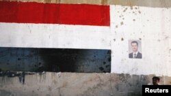 បុរស​ម្នាក់​អង្គុយ​នៅ​ក្បែរ​រូប​របស់​លោក​ប្រធានាធិបតី​ស៊ីរី Bashar al Assad ក្នុង​ពេល​បើក​ផ្លូវ​ចម្លោះ​ពី ក្រុង Homs ទៅ​ក្រុង Hama ឡើង​វិញ នៅ​ក្នុង​ប្រទេស​ស៊ីរី កាលពី​ថ្ងៃទី៦ ខែមិថុនា ឆ្នាំ២០១៨។