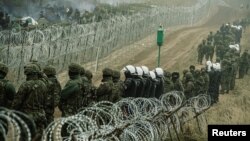 Polish soldiers and police watch migrants at the Poland/Belarus border near Kuznica, Poland, November 11, 2021, in this photograph released by the Territorial Defence Forces. 