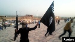 FILE - An Islamic State fighter holds an IS flag and weapon on a street in Mosul, Iraq, in June 2014.