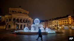 A man passes by the illuminated fountain in front of the Old Opera in Frankfurt, Germany, Dec. 10, 2020.