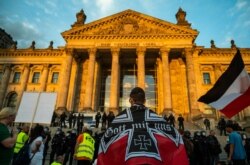 FILE - A demonstrator wrapped in a flag of the German empire faces off with riot policemen standing guard at the Reichstag building, which houses the Bundestag lower house of parliament, after protesters tried to storm it, in Berlin, Aug. 29, 2020.