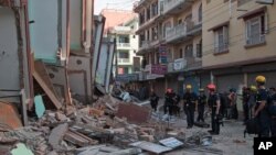 Para petugas keselamatan berdiri di samping gedung yang ambruk akibat gempa di Kathmandu (12/5). (AP/Ranup Shrestha)