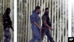 Police officers escort a man in a blue overall along a corridor at the German Federal Supreme Court in Karlsruhe, Germany, March 3 2011. German investigators said they suspected a Kosovan man arrested for the fatal shooting of two US airmen on their bus 
