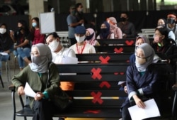 FILE - Employees working at AEON Shopping Mall sit spaced apart as they wait for their turn to take a coronavirus test in Tangerang on the outskirts of Jakarta, Indonesia, Aug. 7, 2020.