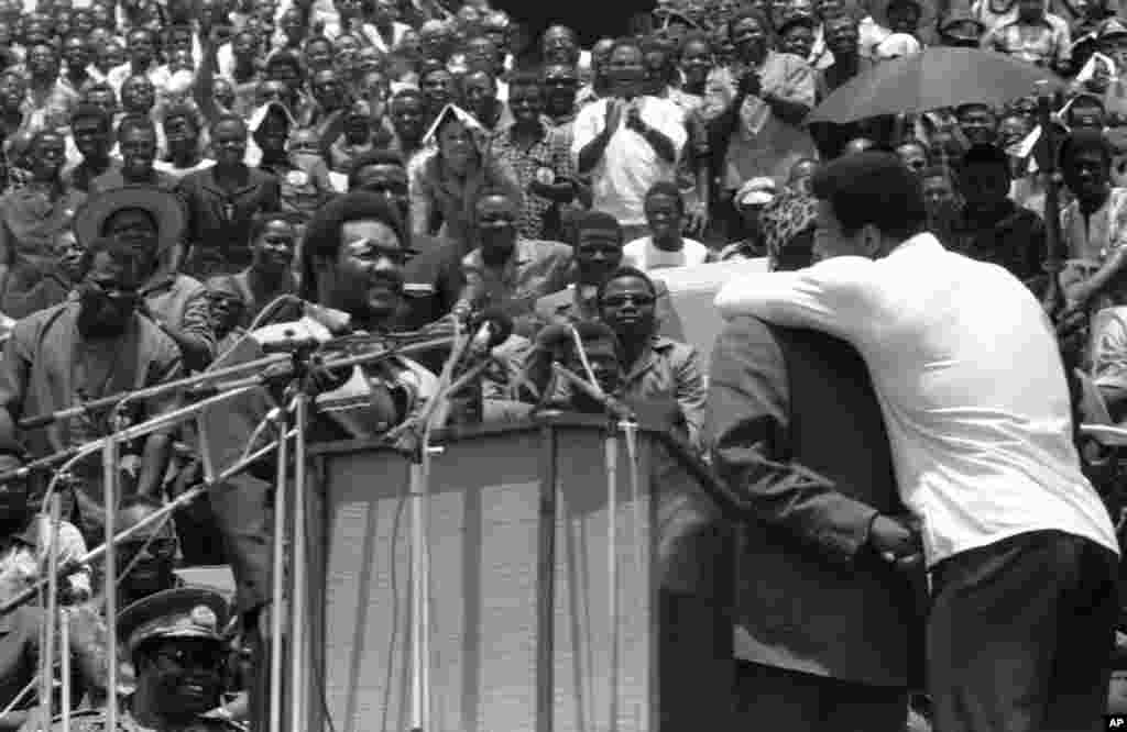 Muhammad Ali embrasse le président du Zaïre Mobutu Sese Seko sur la joue comme le président le présente à la foule à Kinshasa, au Zaïre, le 22 septembre 1974. À gauche, un George Foreman amusé, qui a serré la main du président plus tard. Les deux boxeurs ont assisté aux cérémonies d&#39;ouverture d&rsquo;un festival&nbsp; au stade du 30 mai, où ils vont se battre pour le titre des poids lourds le 30 octobre 1974. (AP Photo / Horst Faas) 