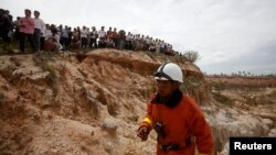 Petugas penyelamat di lokasi tempat helikopter militer Kamboja jatuh di pinggir Phnom Penh, sementara warga mengawasi (14/7). 