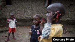 Olematu, 3, center, and Ibrahim, 4, talk on toy phones in a village near Kenema, Sierra Leone. Their 15-year-old sister, Betty, has taken charge after their mother’s death from Ebola. Betty survived an Ebola infection. (© UNICEF / Bindra) 