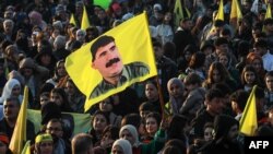 Seorang wanita Kurdi Suriah mengibarkan bendera bergambar pendiri Partai Pekerja Kurdistan Abdullah Ocalan, dalam acara di Kota Qamishli yang mayoritas penduduknya Kurdi di timur laut Suriah untuk mendengarkan pesan dari pemimpin PKK yang dipenjara, 27 Februari 2025. (Foto: AFP)