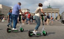 FILE - People use electric scooters by California-based bicycle rental service Lime at the Brandenburg Gate in Berlin, Germany, June 21, 2019.