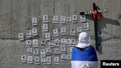 A demonstrator wearing the national flag looks at pictures of protesters who died during the protests against Nicaraguan President Daniel Ortega's government last year, after a religious service at the Metropolitan Cathedral in Managua, Nov. 2, 2019.