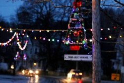 A lit Christmas tree hangs from a pole at dusk as holiday lights illuminate downtown in Farmington, N.H., March 19, 2020.