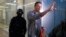 Russian opposition leader Alexei Navalny speaks to the media as a policeman stands guard at the Foundation for Fighting Corruption office in Moscow, Russia, Dec. 26, 2019.