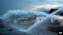 FILE - A police officer keeps an eye on demonstrators as a water canon clears barricades in the Nyakabyga district of Bujumbura, Burundi, May 8, 2015. 