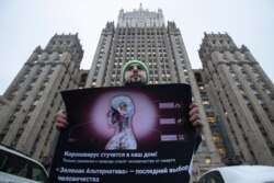 Andrei Nikolayev, an activist of the Green Alternative party holds a banner during one-man protest picket outside the Foreign Ministry headquarters building, in the background, to call on officials to do more to prevent the spread of the new virus