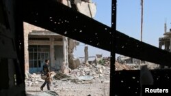 Seorang pejuang Free Syrian Army membawa senjatanya seraya melintasi gedung-gedung yang hancur di bagian selatan kota Deraa, Suriah yang dikuasai pemberontak pada tanggal 9 Juli 2017 (foto: REUTERS/Alaa Al-Faqir) 