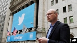 A man uses a mobile phone as he walks past the New York Stock Exchange ahead of Twitter IPO on November 7, 2013, in New York. 