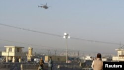 Afghan security forces keep watch as a NATO helicopter flies over at the site of an attack in Jalalabad December 2, 2012. Suicide attackers detonated bombs and fired rockets outside a major U.S. base in Afghanistan on Sunday, killing five people in a braz