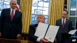 President Donald Trump shows off an executive order to withdraw the U.S. from the Trans-Pacific Partnership trade pact, Jan. 23, 2017, in the Oval Office of the White House in Washington.